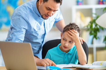 caring father helps his son with homework, using a laptop during distance learning. A parent...