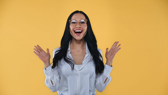 amazed businesswoman in eyeglasses showing wow gesture isolated on yellow
