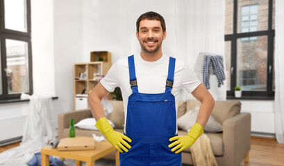 profession, cleaning service and building concept - happy smiling male worker or cleaner in overall and gloves over home room background