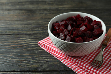 Bowl with beet salad, fork and kitchen towel on wooden background