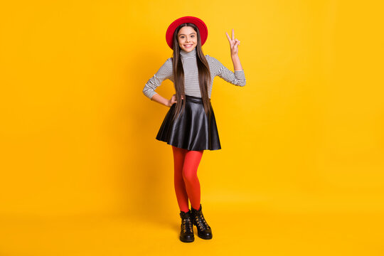 Photo of charming pretty young girl dressed leather skirt red headwear showing v-sign isolated yellow color background