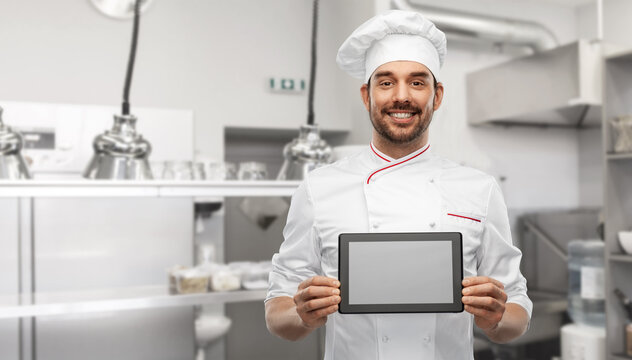 cooking, culinary and people concept - happy smiling male chef in toque showing tablet pc computer over restaurant kitchen background