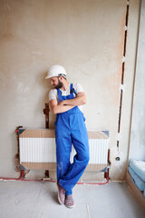 Young handsome plumber installing water radiator in unfinished apartment