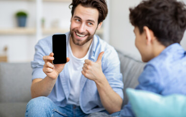 Like this app. Happy young father showing smartphone with blank black screen to his son and showing...