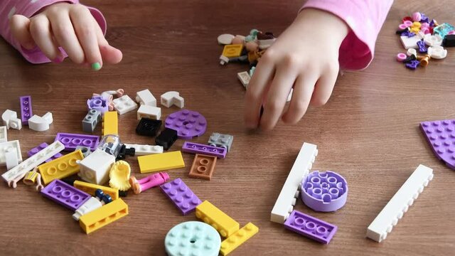 Child hands play with colorful plastic toy bricks and constructor game blocks. Toddler girl hands touch and rotate tiny playthings on wooden table