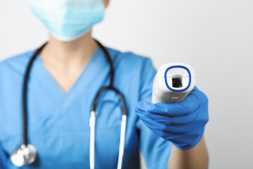 Doctor with infrared thermometer on light background, closeup. Checking temperature during Covid-19 pandemic