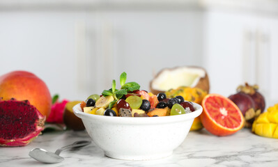 Delicious exotic fruit salad and ingredients on white marble table in kitchen