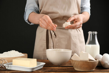 Woman with compressed yeast and dough ingredients at wooden table, closeup