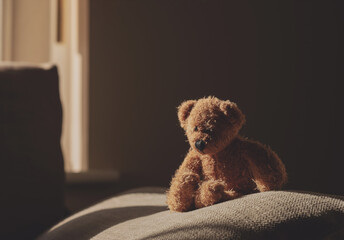 Dramatic photo of Teddy bear is sitting on sofa in the dark room with sunlight shining from window,lowkey light shot of Lonely teddy sitting alone in living room  international missing children's day