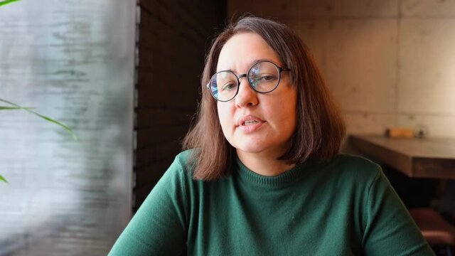Pretty woman sitting in cafe and talking. Green dress with long sleeves. Casual lifestyle portrait. Business female person interview professional. Vlog slow video