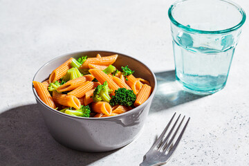 Red lentil pasta with broccoli in gray bowl. Healthy vegan pasta with vegetables.