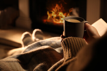 Woman with cup of drink near fireplace at home, closeup