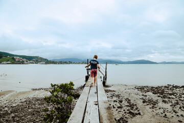 Boy walking along old jetty at Mandalay with view of Airlie Beach across the bay. Queensland tourist adventure.