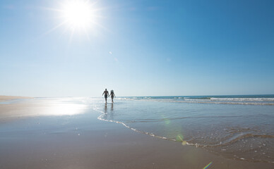Honeymoon couple holding hands walking on a lonely beach. Newlyweds relaxing on summer vacation. Travel vacation and love concept