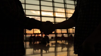 silhouette of two business people handshake in airport sunset light. Two man meet after arrival in airport. - Powered by Adobe