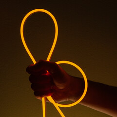 Flexible orange led tape neon in hand on black background