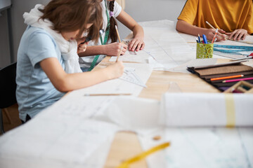 Female children drawing sewing patterns in workshop