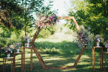 Modern hexagon wedding arch decorated with flowers for  wedding ceremony in the nature.