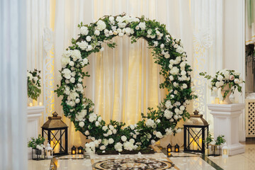 Wedding decor with round arch with flowers and candles on the floor. Arch of foliage and white...