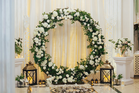 Wedding decor with round arch with flowers and candles on the floor. Arch of foliage and white flowers.