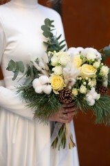 Close up of wedding bouquet in the hands of the bride. Bouquet of pine, eucalyptus, cotton, white roses and lagurus. Trendy bouquet.