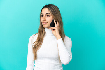 Young caucasian woman using mobile phone isolated on blue background looking to the side