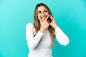 Fototapeta premium Young caucasian woman using mobile phone isolated on blue background happy and smiling