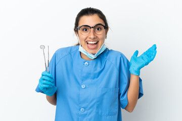 Young woman dentist holding tools isolated on white background with shocked facial expression