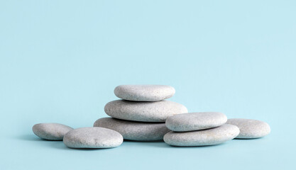 Obraz na płótnie Canvas Minimalist beauty products background concept. Gray color flat sea stones stacked like an pedestal lot of copy space on blue background.