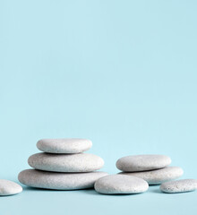 Fototapeta na wymiar Minimalist beauty products background concept. Gray color flat sea stones stacked like an pedestal lot of copy space on blue background.