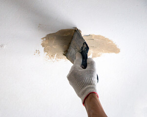 mans hand in cloth glove with spatula and putty, applies mastic to the wall, ceiling to level the...