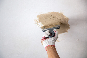 mans hand in cloth glove with spatula and putty, applies mastic to the wall, ceiling to level the...
