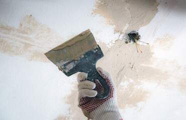 mans hand in cloth glove with spatula and putty, applies mastic to the wall, ceiling to level the...