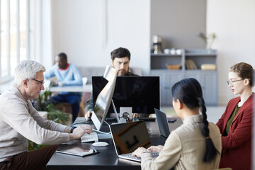 Side view at diverse group of business people working with computers in modern office, focus on senior man in IT studio
