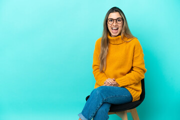 Young caucasian woman sitting on a chair isolated on blue background with surprise facial expression