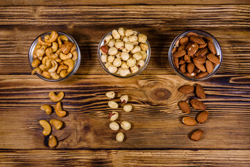 Various nuts (almond, cashew, hazelnut) in glass bowls on a wooden table. Vegetarian meal. Healthy eating concept. Top view