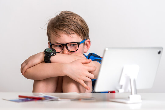 Angry And Stressed Little Kid Boy Sitting At The Table With Laptop. Alone Child On His Online Lesson During Quarantine And Coronavirus Outbreak. Work From Home.