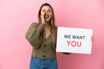 Young caucasian woman isolated on pink background holding We Want You board and shouting