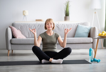 Full length of mature woman meditating with closed eyes, making gyan mudra with her hands at home