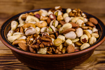 Various nuts (almond, cashew, hazelnut, pistachio, walnut) in ceramic plate on a wooden table. Vegetarian meal. Healthy eating concept