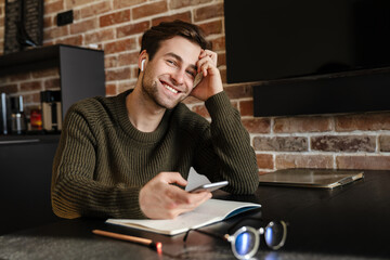 Smiling brunette man using phone and taking notes