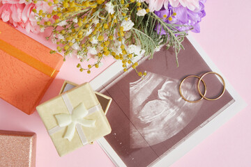 ultrasound shot on pink background, flowers and gift box for decor, pregnancy and motherhood concept, conscious parenthood
