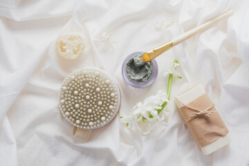 wooden massage brush, hyacinth and tulip flowers, soap bar and blue clay in a jar on a white cloth eco friendly spa concept