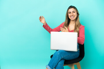 Naklejka premium Young caucasian woman sitting on a chair with her pc isolated on blue background making guitar gesture