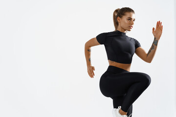 Determined muscular female athlete workout, raising leg and doing stretching exercises. Sport woman in sportswear training indoors, doing fitness aerobics, white background