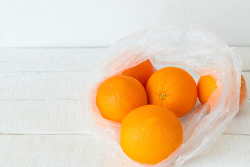 Fresh ripe oranges are in a plastic bag on a white wooden table. Copy space