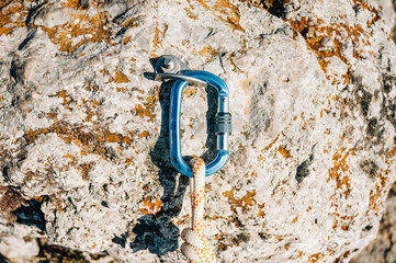 Close Up of climbing gear, Anchor, Rope, and Carabiner with cliff rock as a backdrop.