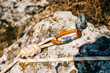 Close Up of climbing gear, Anchor, Rope, and Carabiner with cliff rock as a backdrop.