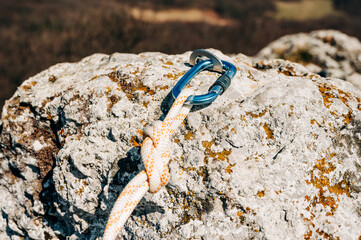 Close Up of climbing gear, Anchor, Rope, and Carabiner with cliff rock as a backdrop.