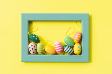 colorful painted easter eggs in a turquoise frame on yellow background